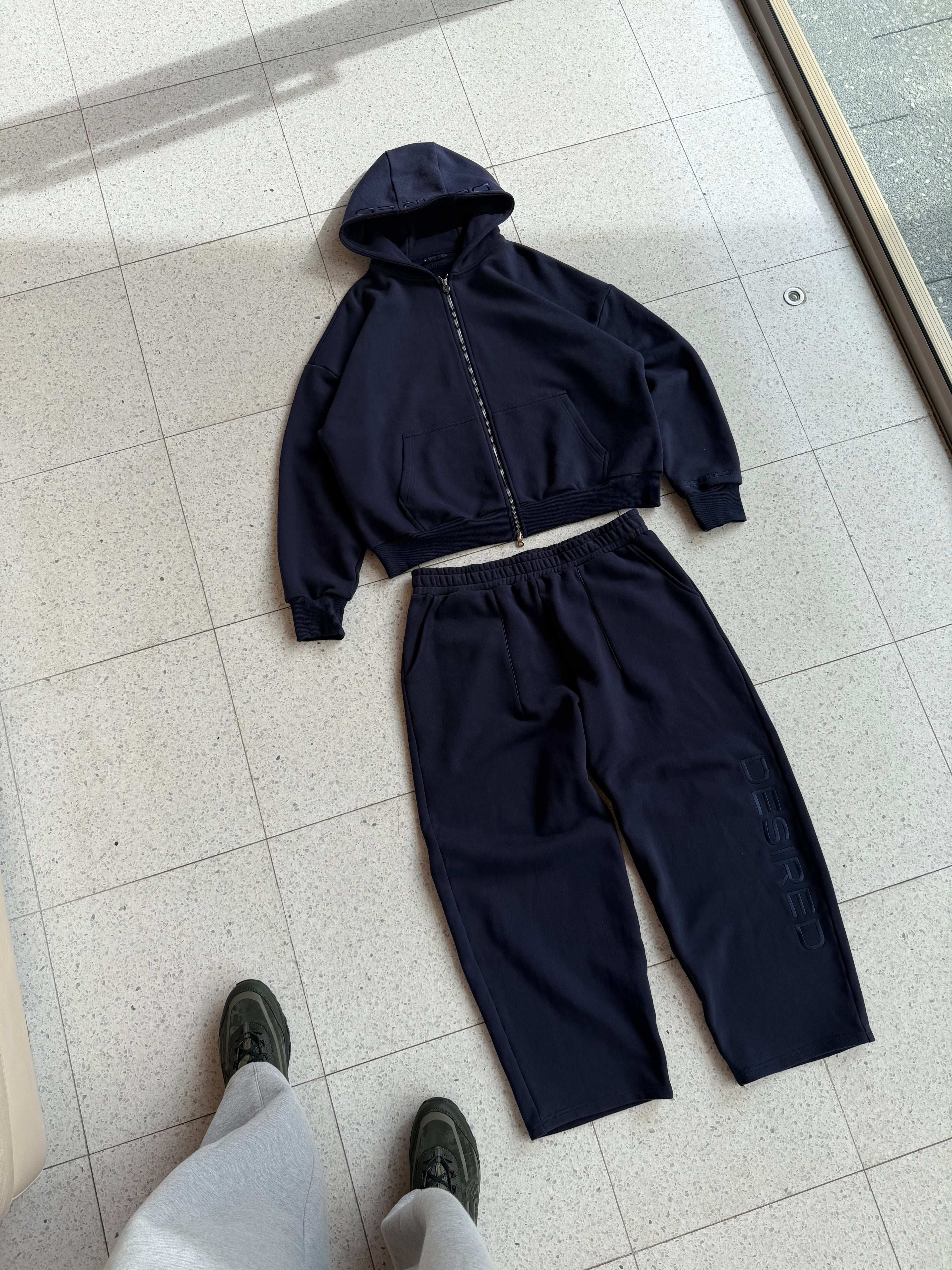 Navy blue tracksuit on a tiled floor with a person's legs visible.